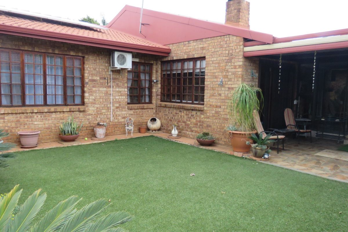 Rear view of a face brick house featuring a paved patio area, artificial lawn, and timber-framed windows.