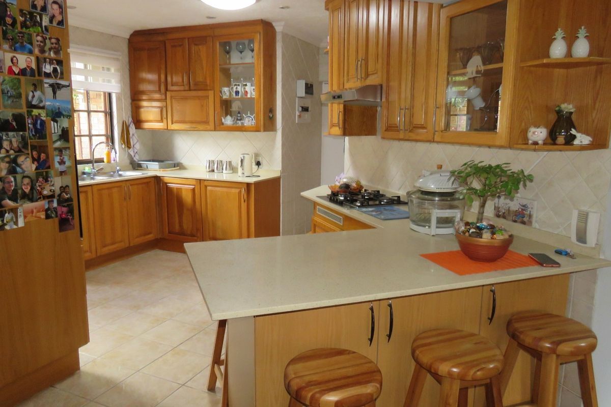 A functional kitchen featuring wooden cabinetry, stone countertops, a gas hob with extractor, and a breakfast bar area with tiled flooring.