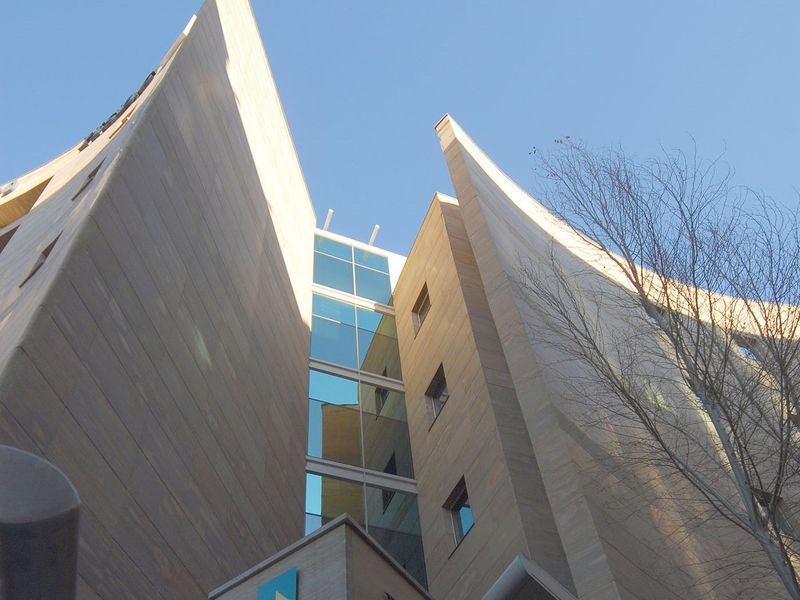 Low angle view of a modern commercial building facade featuring stone cladding and a central glass curtain wall section.