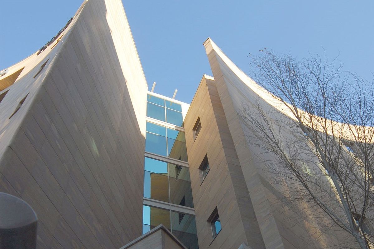 Low angle view of a modern commercial building facade featuring stone cladding and a central glass curtain wall section.