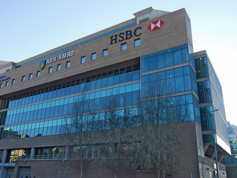 A modern multi-story commercial office building featuring a glass curtain wall facade and stone cladding with prominent corporate signage.