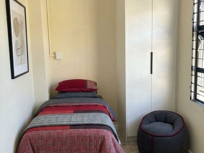 A compact bedroom featuring a built-in wardrobe, tiled flooring, and security bars on the window.