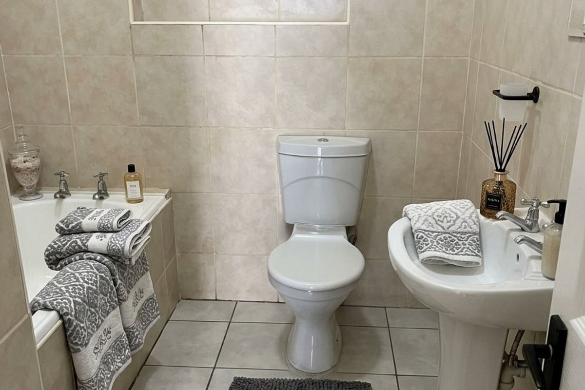 A compact bathroom featuring a built-in bathtub, pedestal sink, and toilet, finished with neutral ceramic wall and floor tiles.