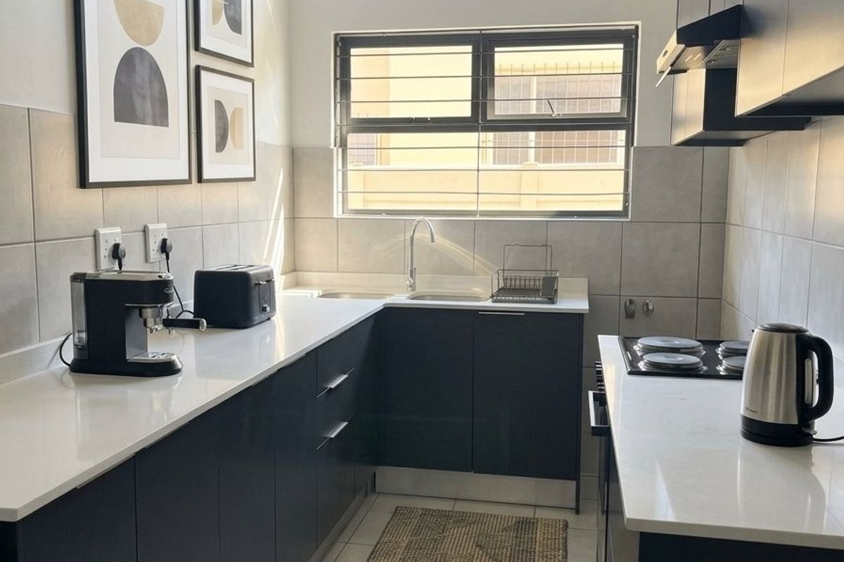 Modern galley-style kitchen featuring dark cabinetry, stone countertops, integrated hob with extractor, and a bright clerestory window for natural light.