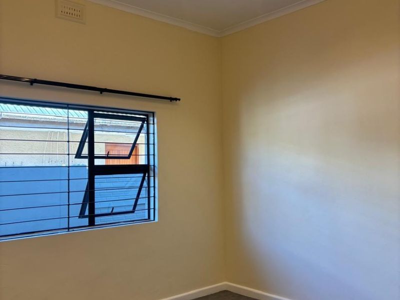 A clean, empty bedroom featuring neutral walls, modern lighting, and a window fitted with security bars.