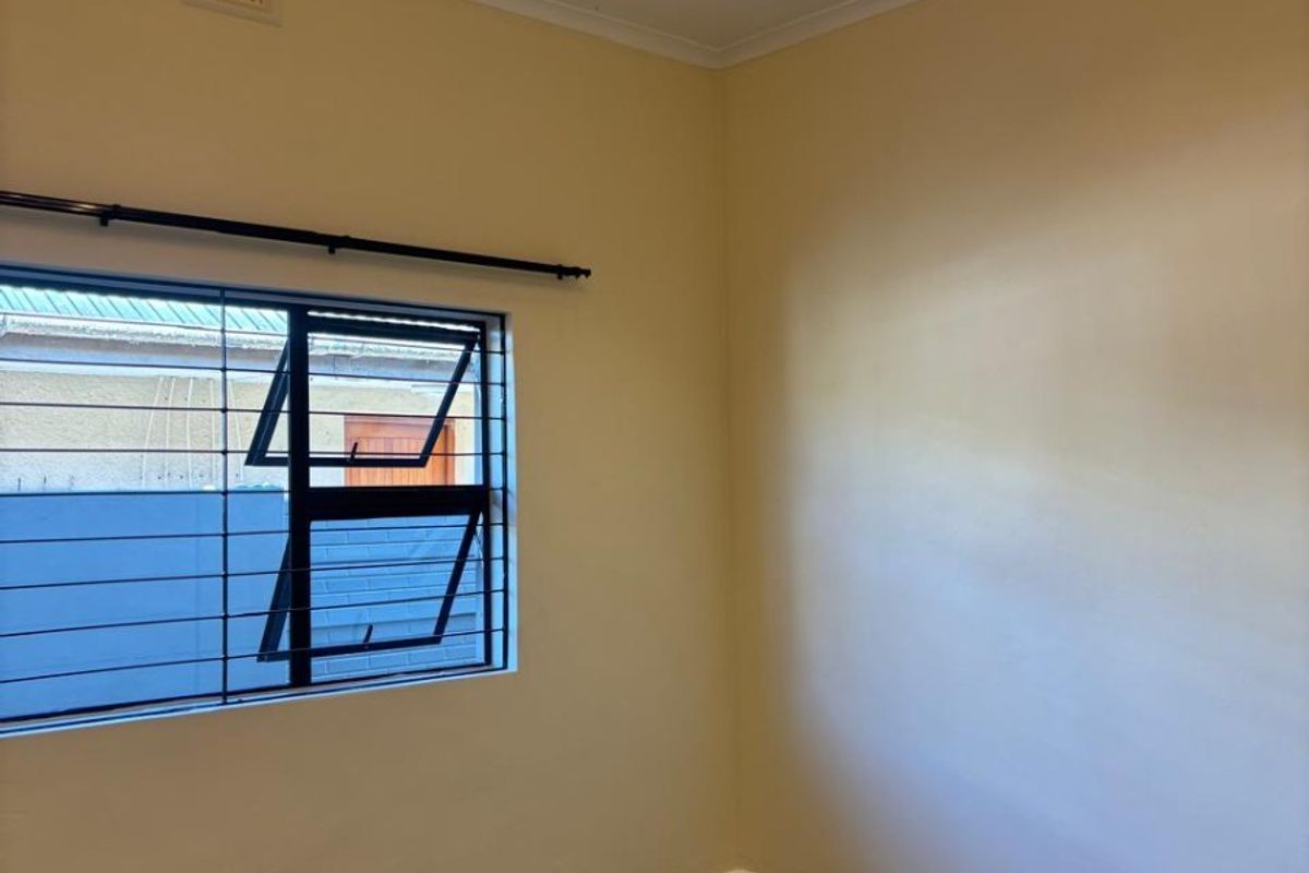 A clean, empty bedroom featuring neutral walls, modern lighting, and a window fitted with security bars.