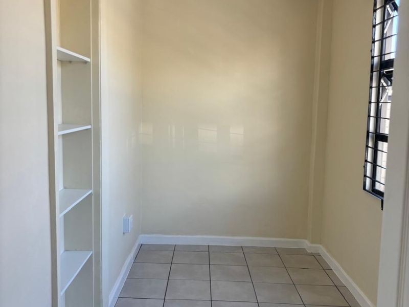 A compact, empty room featuring tiled flooring, built-in wall shelving, and a tongue and groove ceiling, suitable for a small bedroom or home office.
