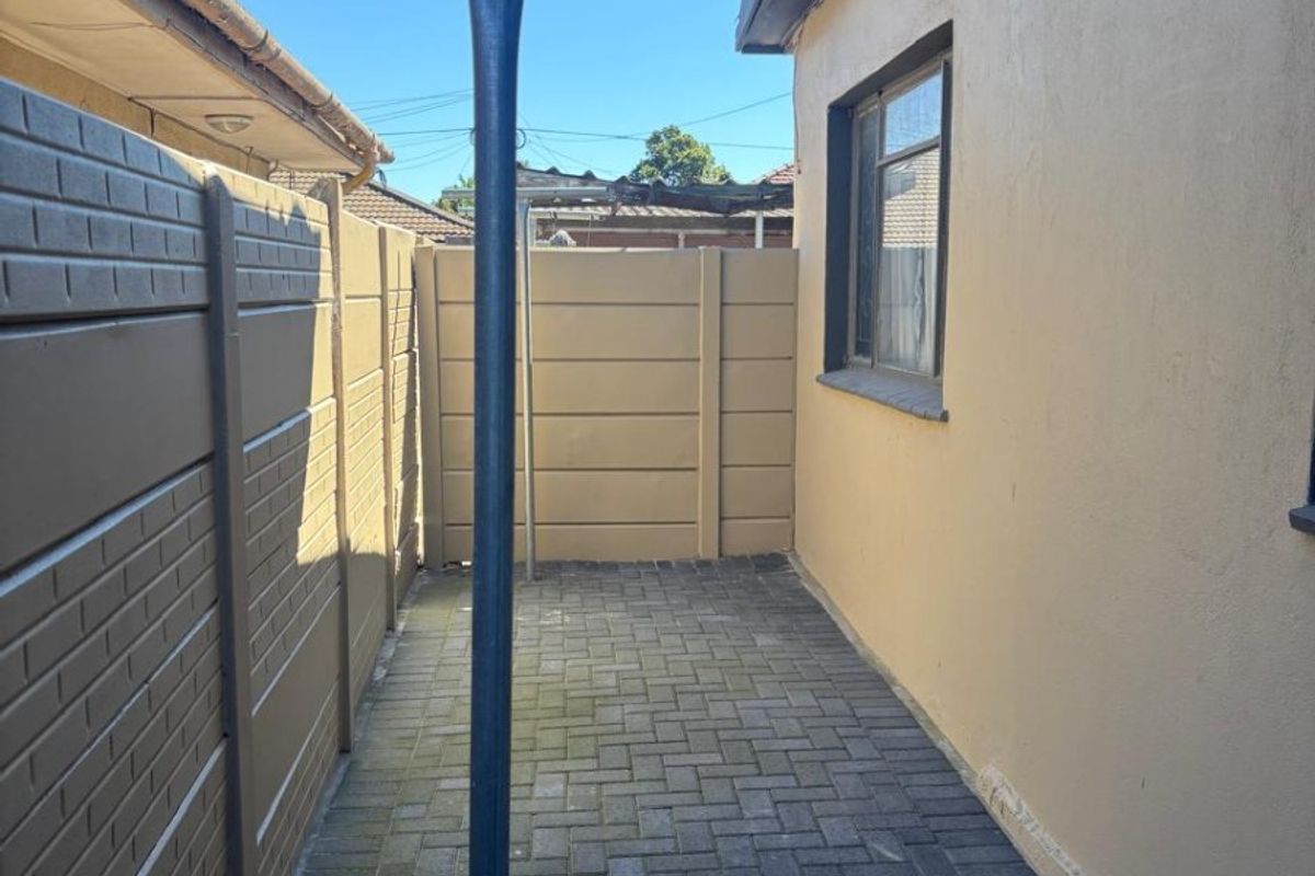 A narrow rear exterior side passage featuring paved flooring, a precast concrete boundary wall, and a fixed metal washing line pole.