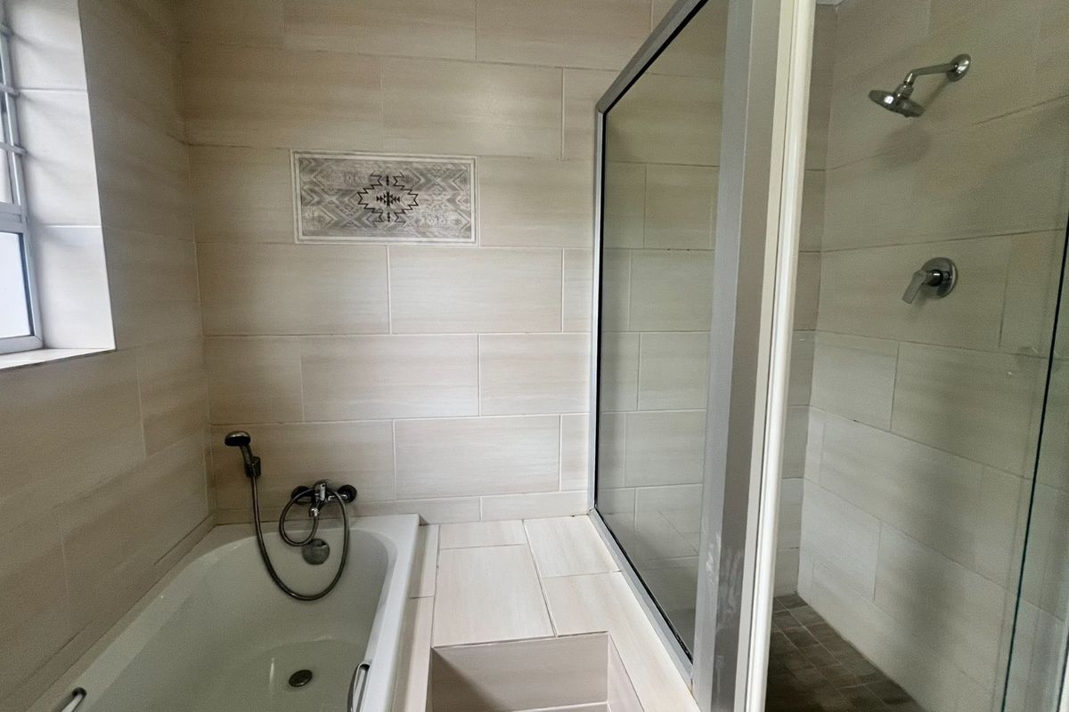 A modern bathroom featuring a built-in bathtub, a separate glass-enclosed shower, and neutral wall tiling.