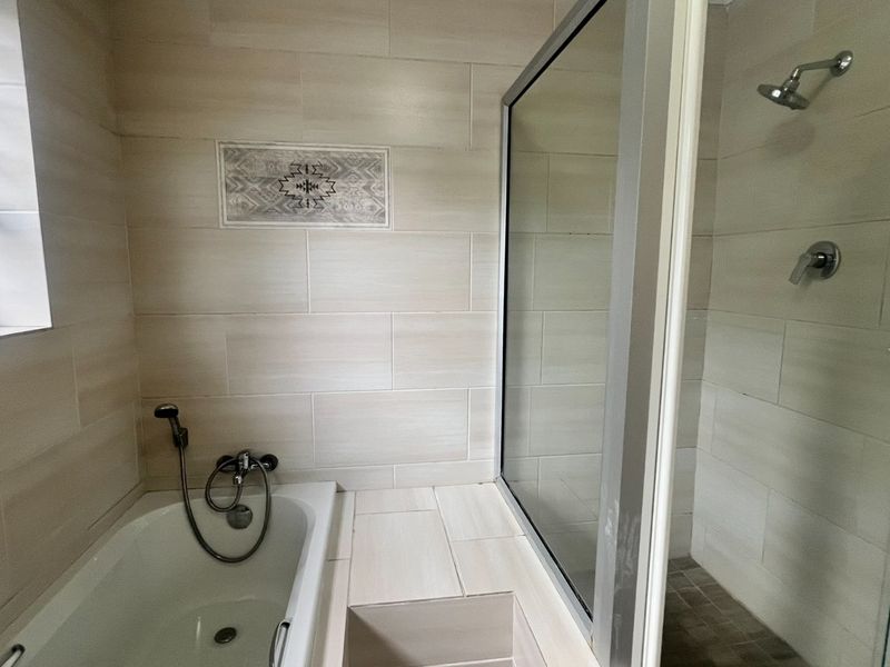 A modern bathroom featuring a built-in bathtub, a separate glass-enclosed shower, and neutral wall tiling.