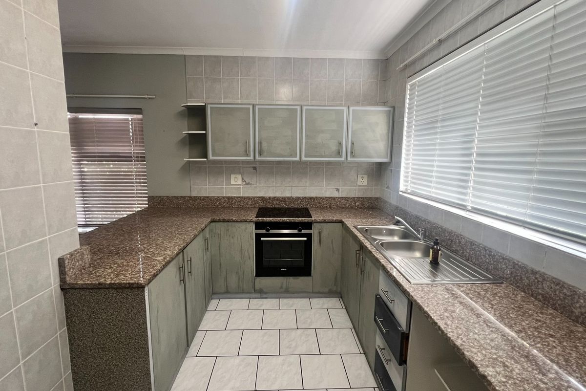 A functional kitchen featuring granite countertops, built-in oven, electric hob, and double stainless steel sink with tiled splashbacks and ample cabinetry.