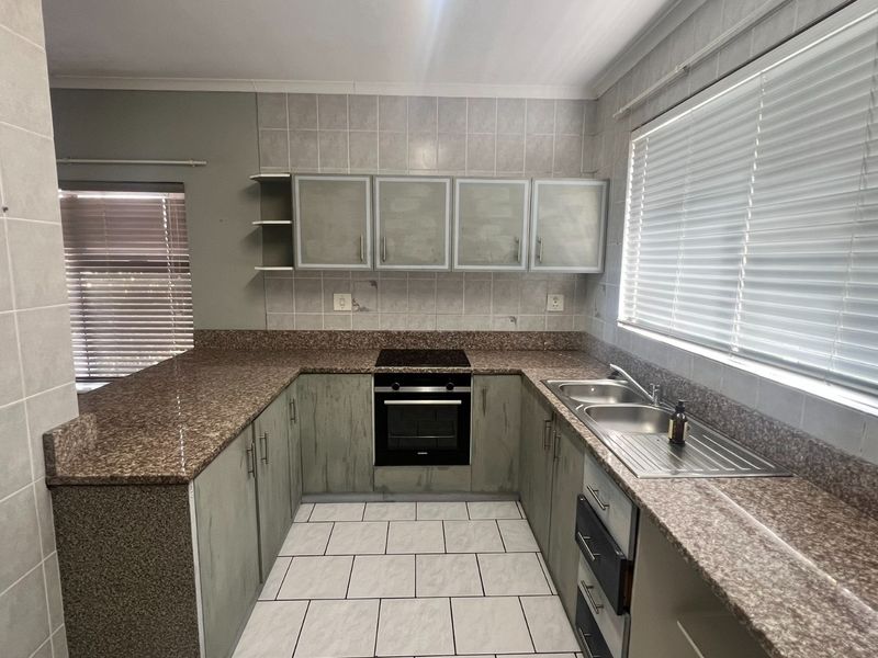 A functional kitchen featuring granite countertops, built-in oven, electric hob, and double stainless steel sink with tiled splashbacks and ample cabinetry.