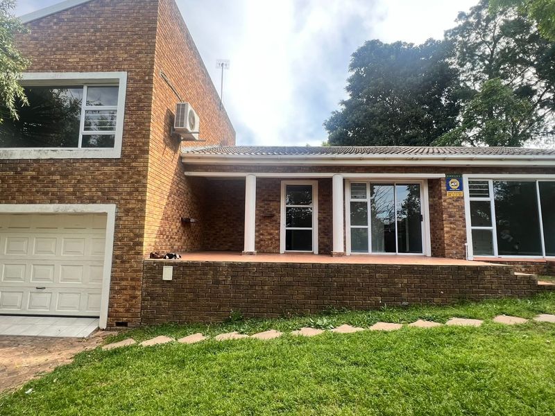 Rear view of a brick cottage featuring a covered patio, sliding glass doors, and an attached garage with a landscaped garden area.