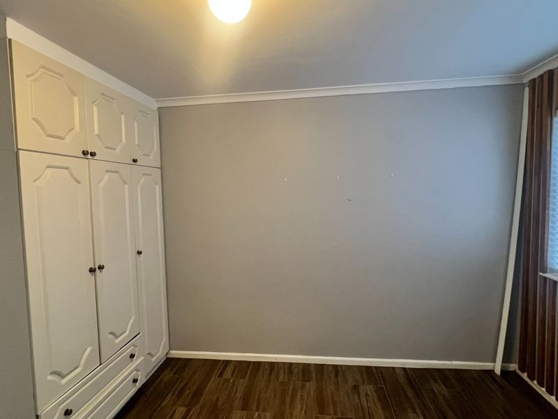 A clean, empty bedroom featuring built-in wardrobes, wood-look laminate flooring, and venetian blinds, offering a neutral canvas for personalization.