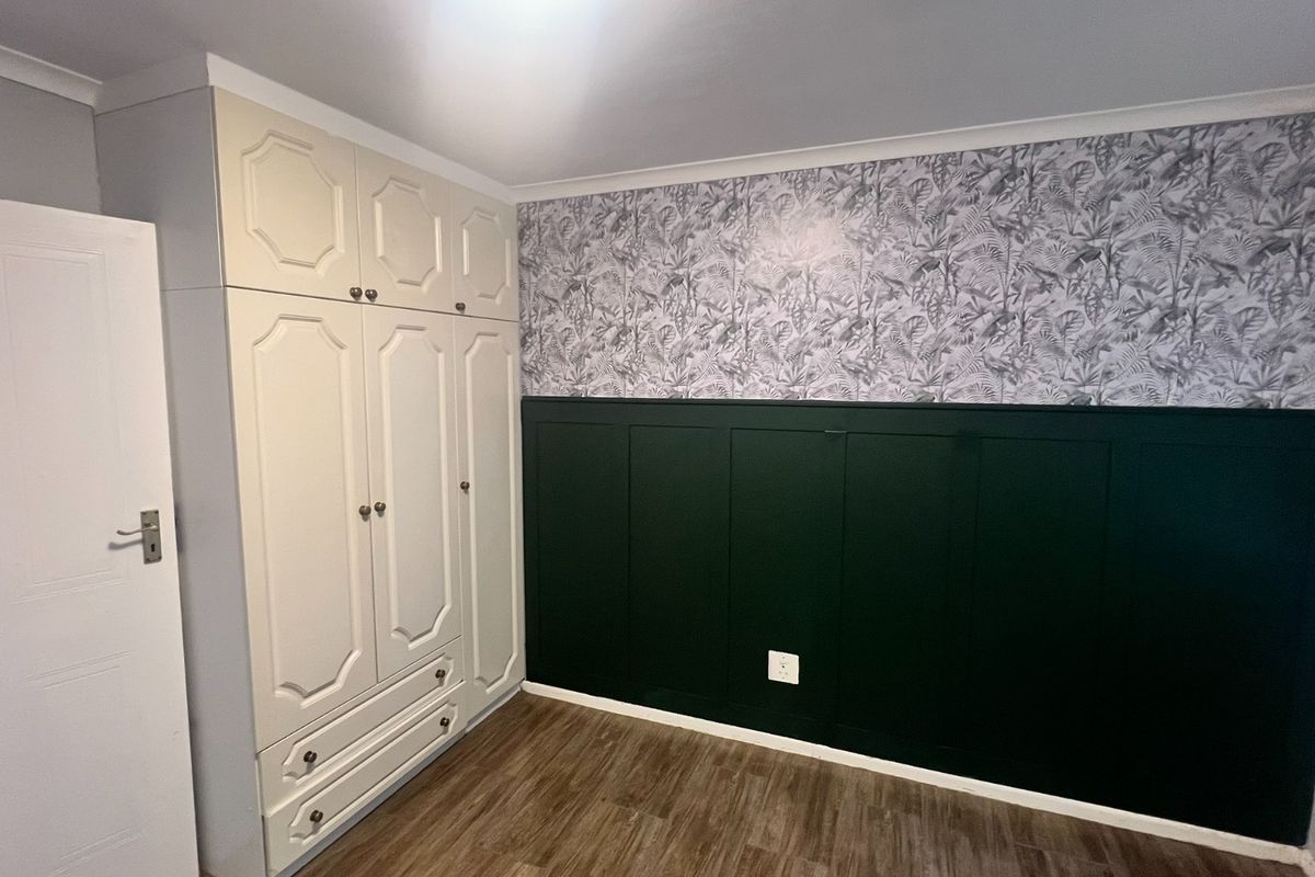 A clean, empty bedroom featuring built-in wardrobes, decorative wainscoting with wallpaper accents, and wood-look laminate flooring.