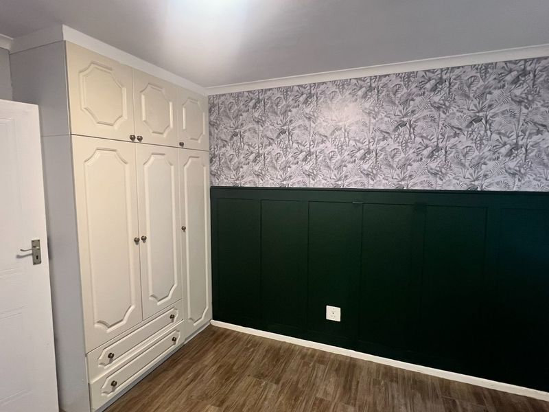A clean, empty bedroom featuring built-in wardrobes, decorative wainscoting with wallpaper accents, and wood-look laminate flooring.