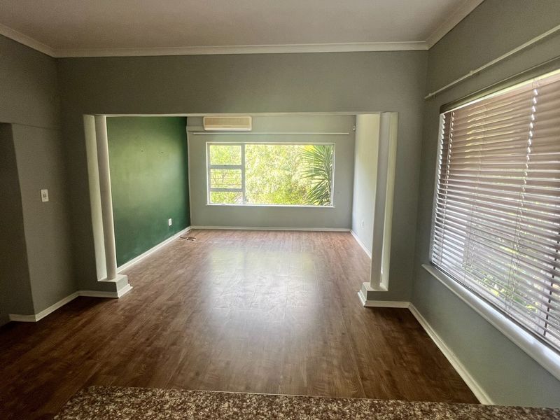 Spacious open-plan living area featuring laminate flooring, an air conditioning unit, and large windows with venetian blinds, offering a bright and versatile layout.