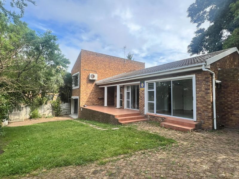 Rear view of a brick cottage featuring a tiled patio, sliding glass doors, and a spacious garden with a paved driveway.