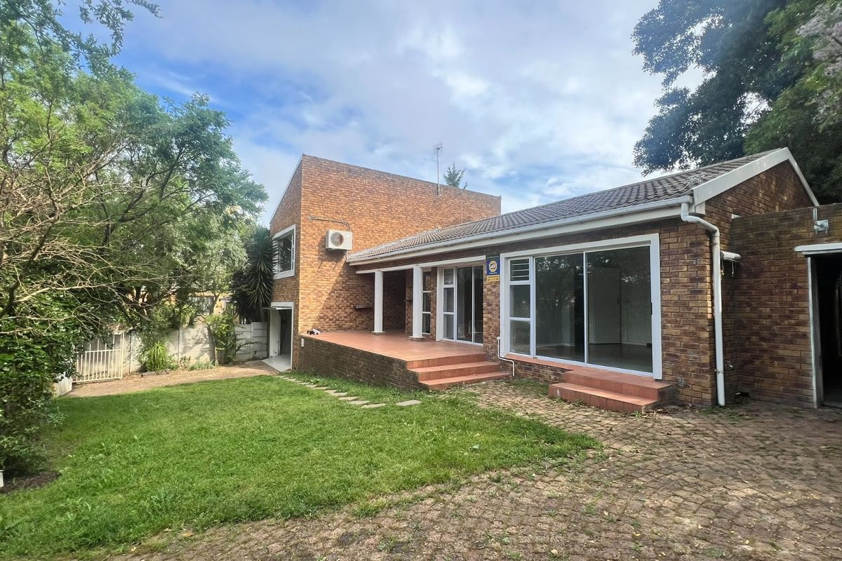 Rear view of a brick cottage featuring a tiled patio, sliding glass doors, and a spacious garden with a paved driveway.