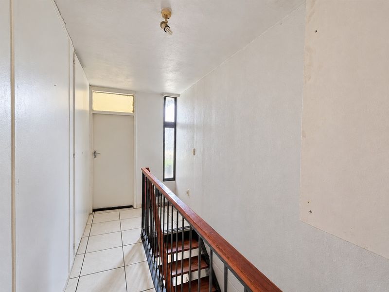 A vacant hallway featuring tiled flooring, a staircase with a wooden handrail, and built-in storage, requiring minor cosmetic updates to the wall finishes.