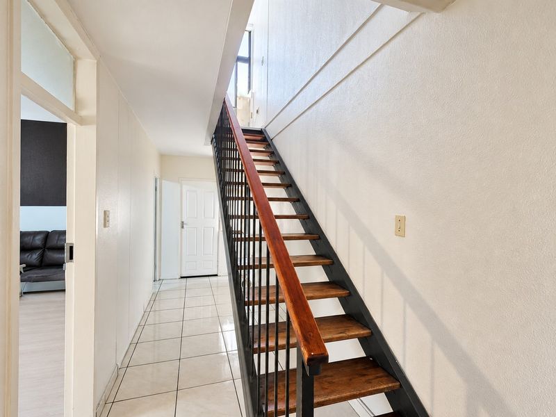 A bright hallway featuring a staircase with wooden treads and a metal balustrade, leading to an upper level with tiled flooring throughout.