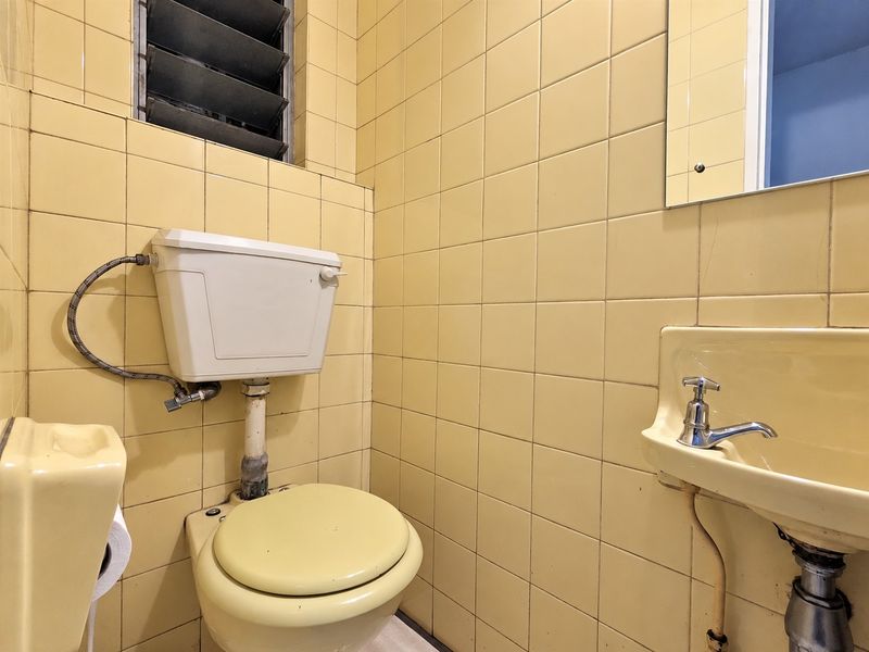 A compact bathroom featuring original yellow wall tiles, a wall-mounted basin, and a louvered window, offering potential for a modern renovation.