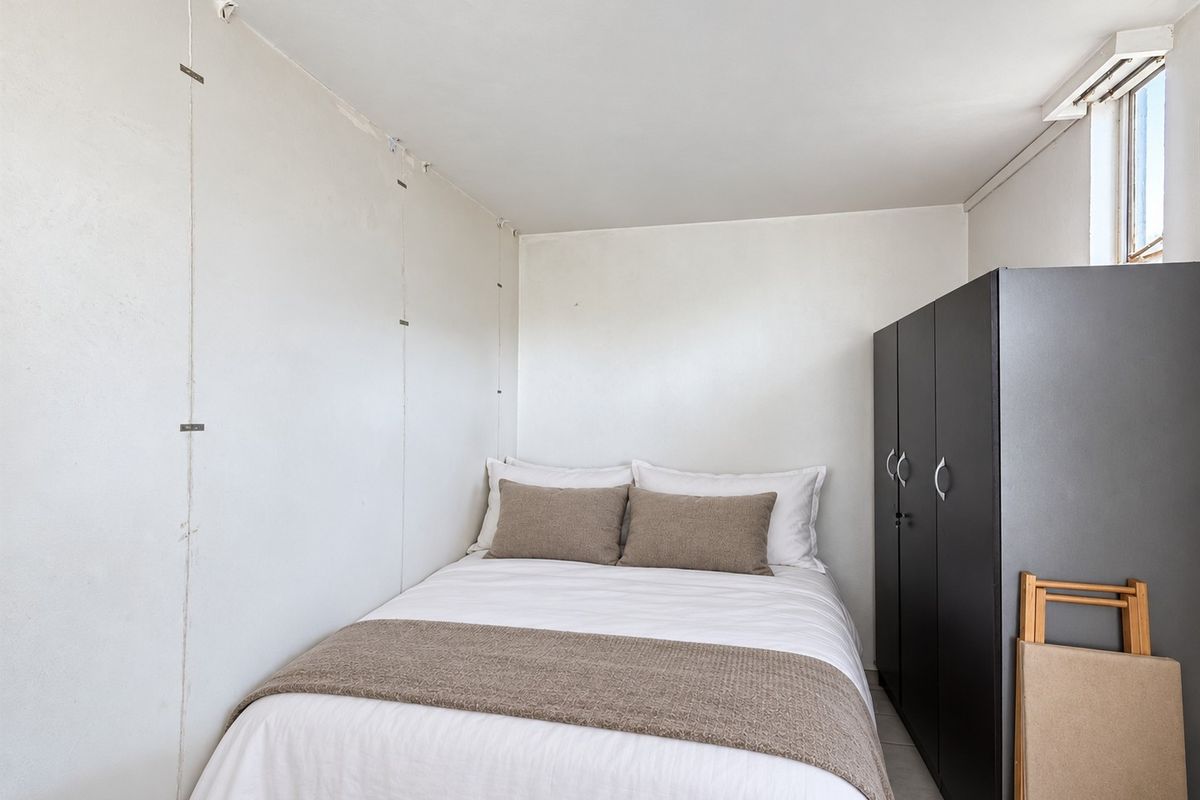 A compact bedroom featuring a built-in wardrobe and plain wall finishes, offering a functional space for rest.