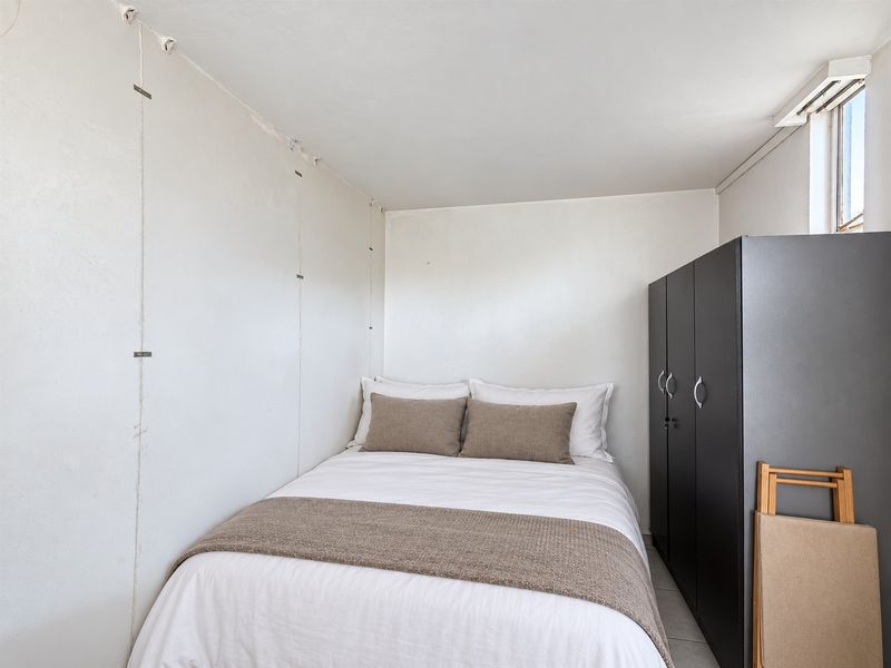A compact bedroom featuring a built-in wardrobe and plain wall finishes, offering a functional space for rest.