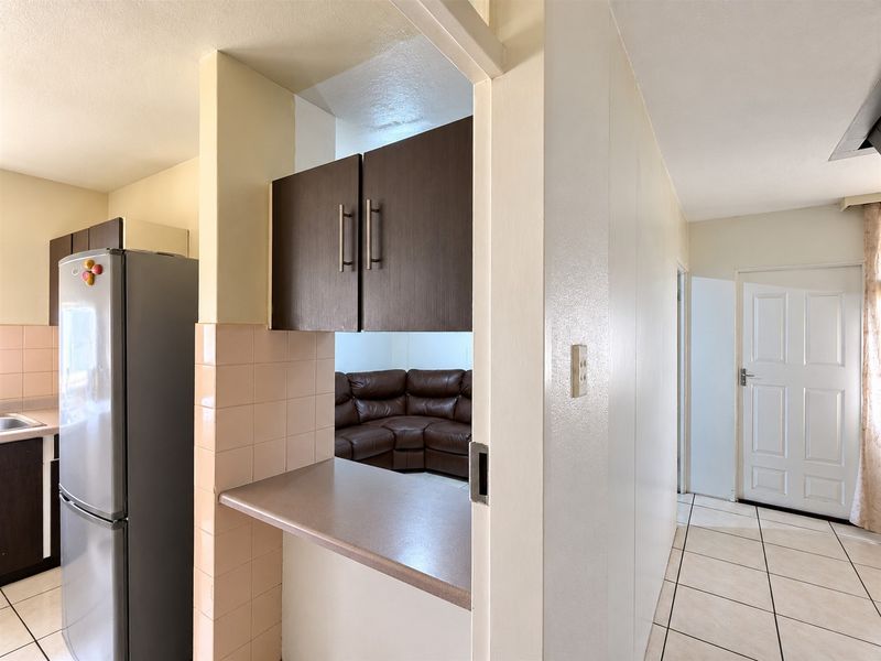 Open plan kitchen area featuring built-in cabinetry and tiled surfaces, connecting to the main living space and entrance hallway.