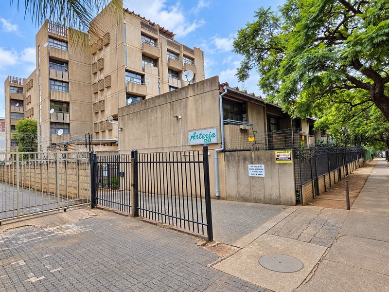 Front exterior view of the Arteria apartment complex, featuring a secure gated entrance, paved driveway, and multi-story concrete building structure.