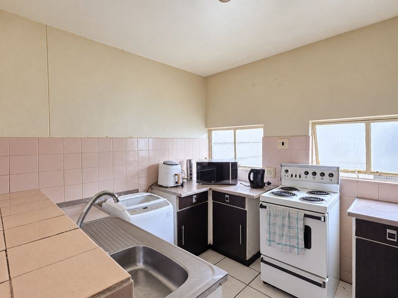A functional kitchen featuring dated cabinetry, tiled splashbacks, a stainless steel sink, and a freestanding stove, offering potential for modernization and renovation.