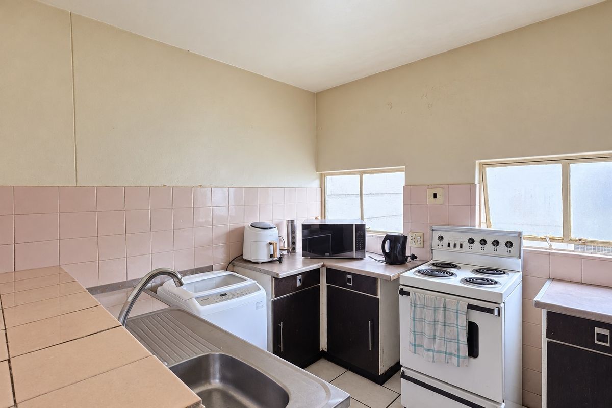 A functional kitchen featuring dated cabinetry, tiled splashbacks, a stainless steel sink, and a freestanding stove, offering potential for modernization and renovation.