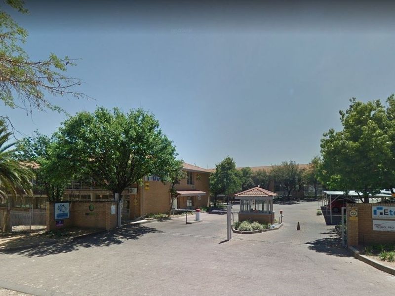 Commercial property entrance featuring a paved driveway, security guard house, boom gate access, and brick building facade with mature landscaping.