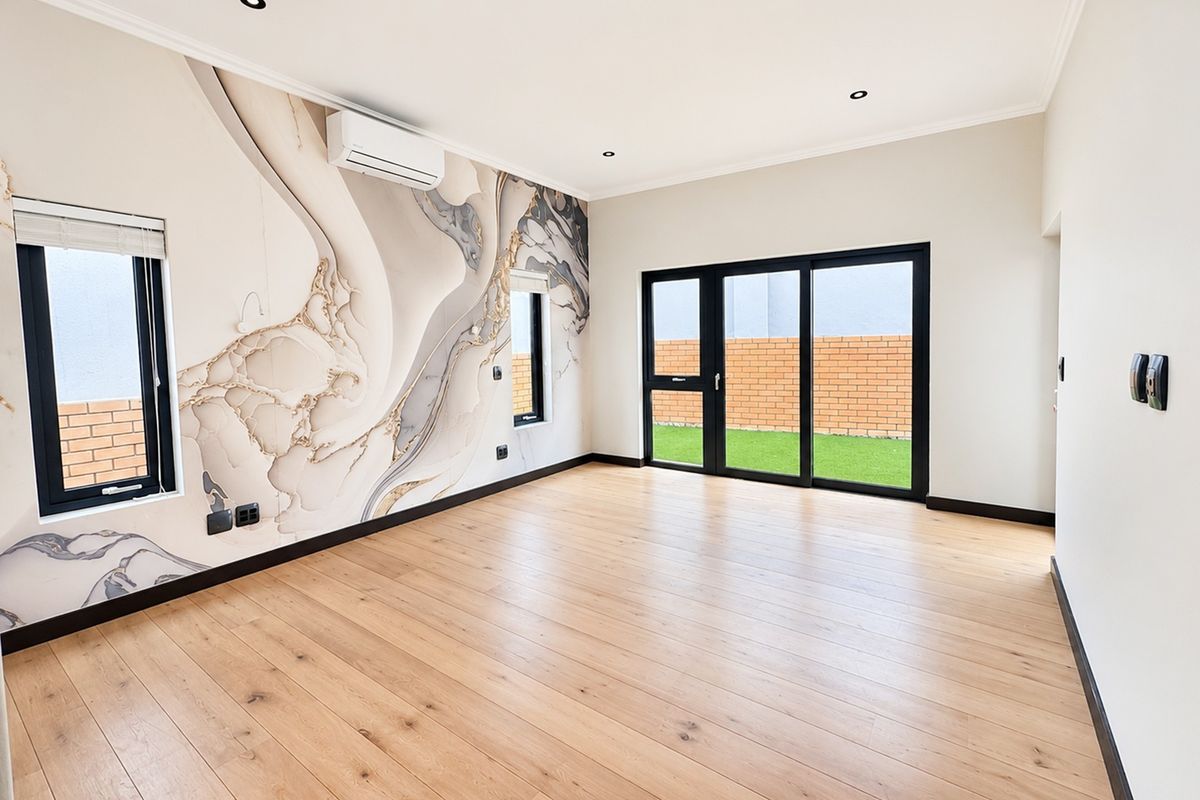 A bright, modern living area featuring engineered wood flooring, a statement feature wall, split-system air conditioning, and sliding glass doors leading to the garden.