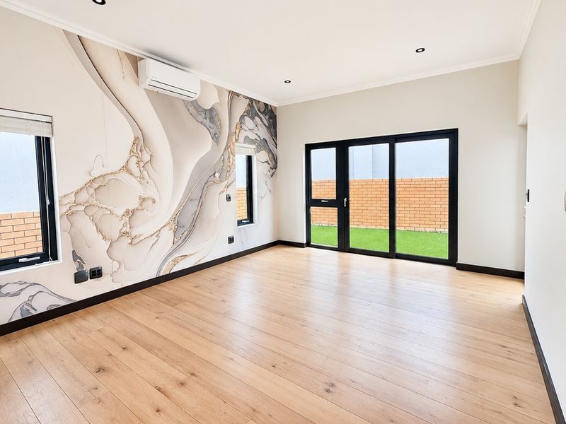 A bright, modern living area featuring engineered wood flooring, a statement feature wall, split-system air conditioning, and sliding glass doors leading to the garden.