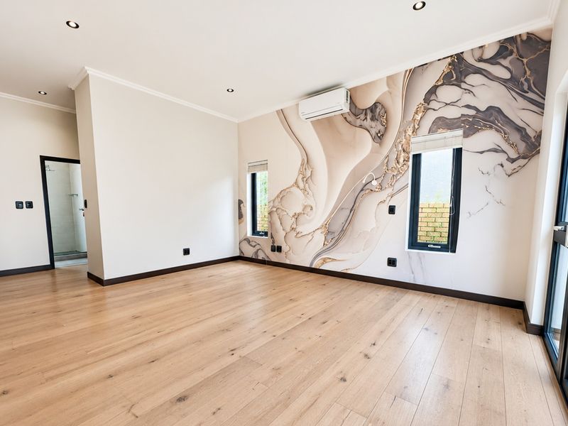 Spacious bedroom featuring light timber flooring, a striking marble-effect feature wall, recessed lighting, and direct access to the outdoors via a sliding glass door.