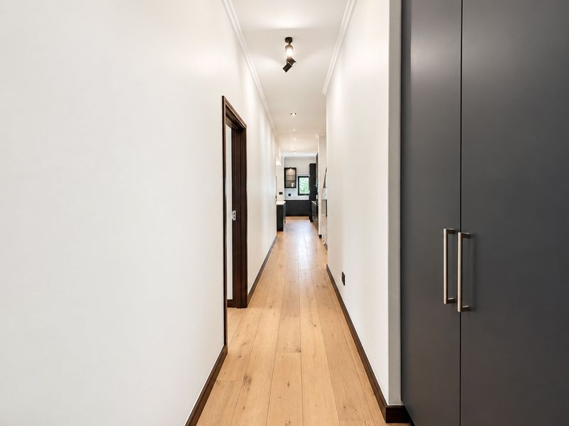 A bright, modern hallway featuring light timber flooring, clean white walls, and sleek built-in storage cabinetry, leading towards the rear of the home.