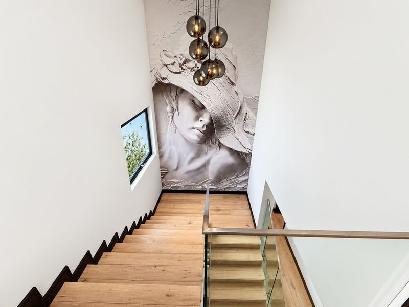 Modern staircase featuring timber treads, a sleek glass balustrade with stainless steel handrail, and a striking feature wall mural.