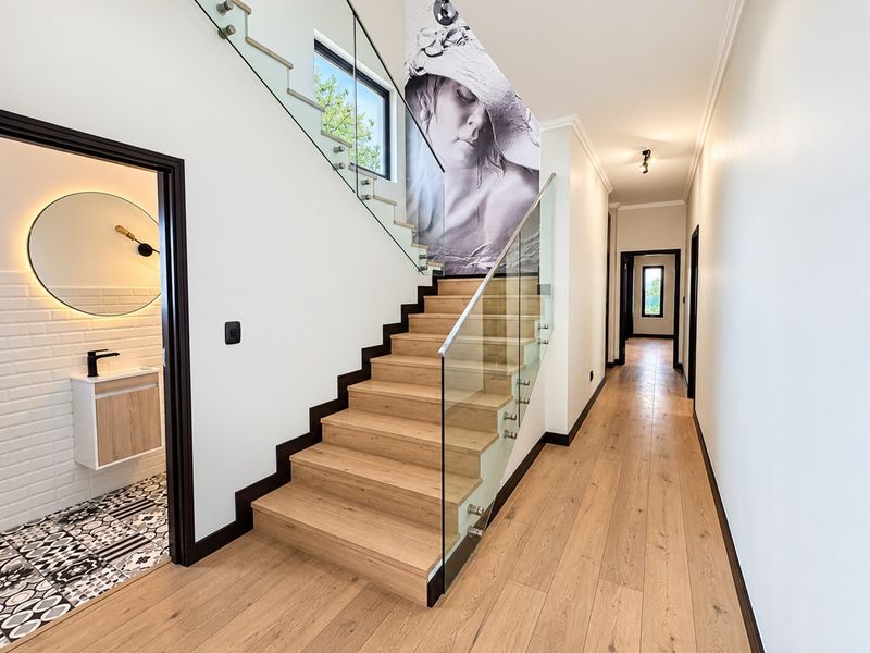 Modern hallway featuring a timber staircase with a glass balustrade, light timber flooring, and access to a contemporary guest bathroom.