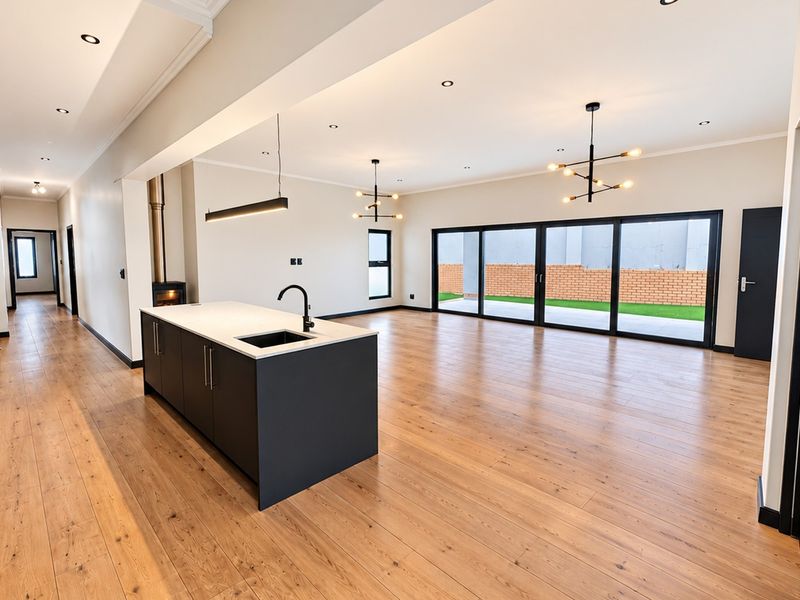 Spacious open-plan living area featuring a modern kitchen island, wood-burning fireplace, timber flooring, and large sliding doors opening to the rear garden.