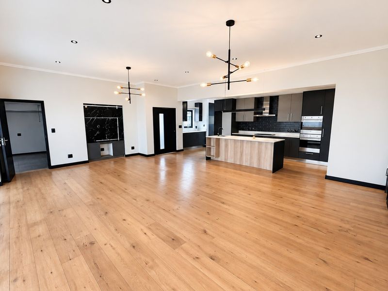 Spacious open-plan living and kitchen area featuring high-quality wood flooring, modern cabinetry, a central island, and contemporary lighting fixtures.