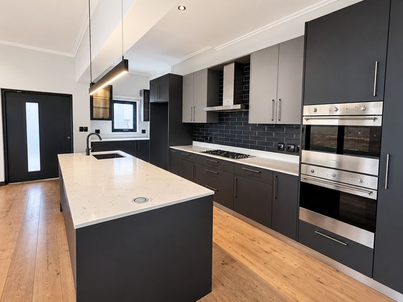 Modern kitchen featuring a large island with stone countertops, dark cabinetry, built-in stainless steel appliances, and a stylish subway tile backsplash.