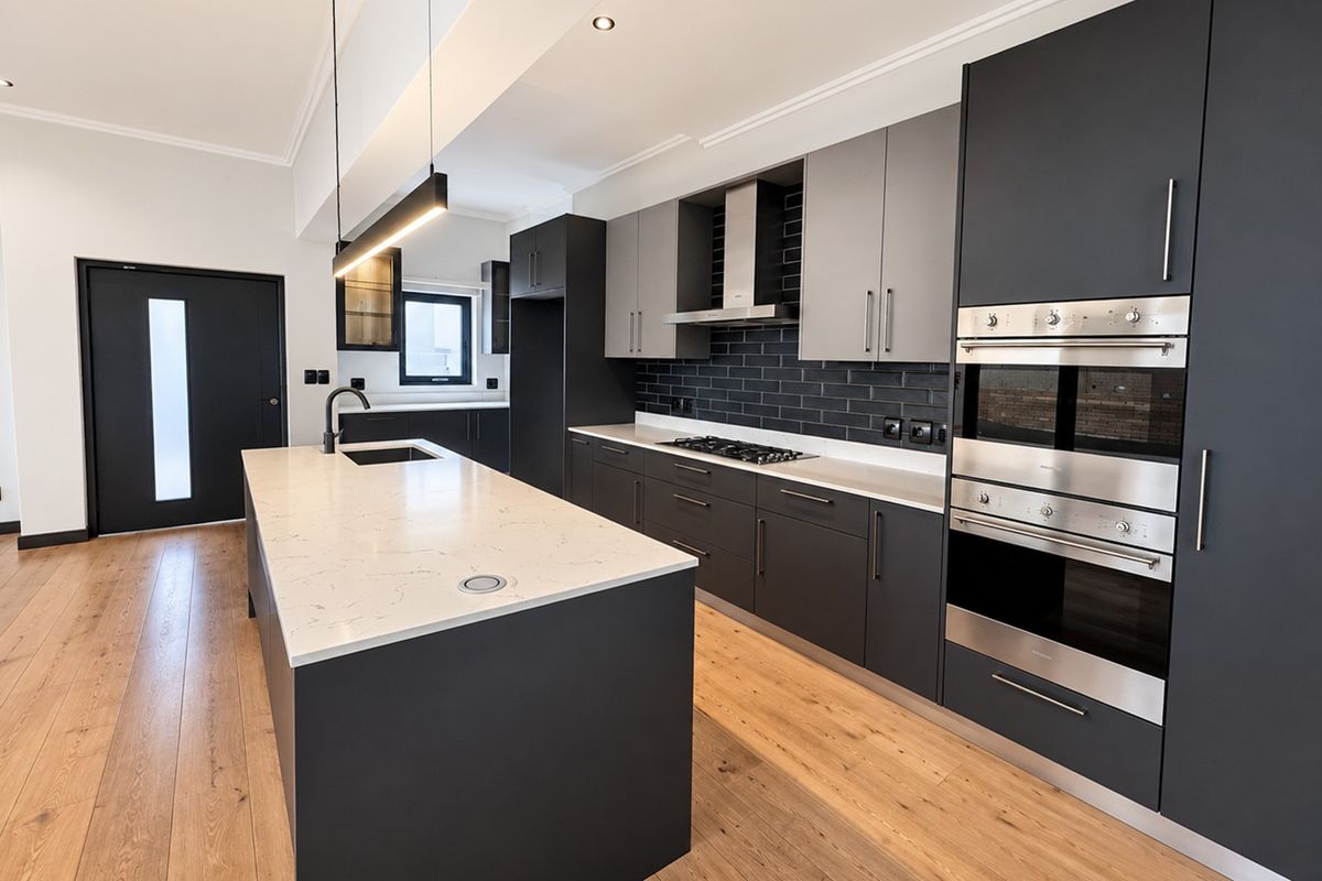 Modern kitchen featuring a large island with stone countertops, dark cabinetry, built-in stainless steel appliances, and a stylish subway tile backsplash.