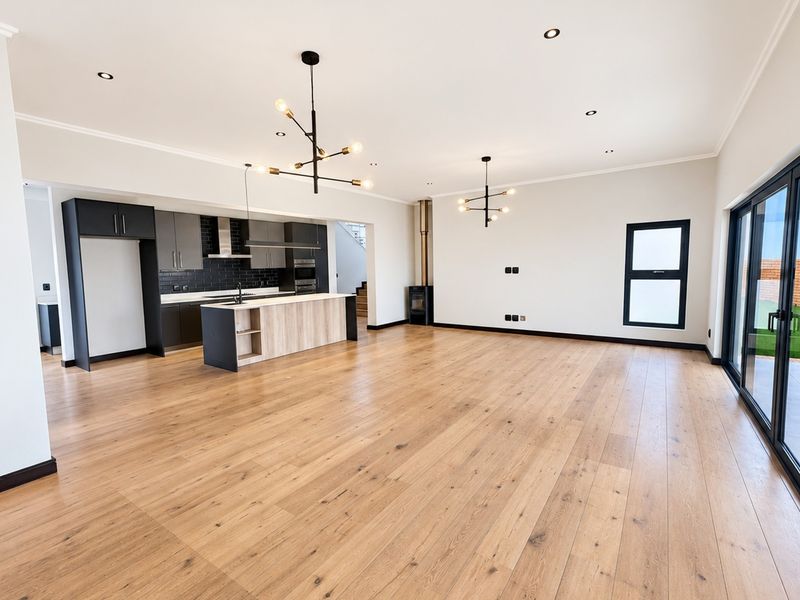 Spacious open-plan living area featuring modern kitchen cabinetry, engineered wood flooring, a fireplace, and large sliding doors leading to the outdoor space.