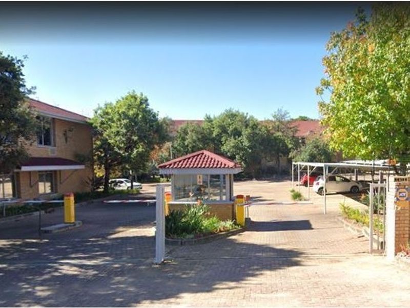 Commercial property entrance featuring a security guard booth, boom gate access control, paved driveway, and covered parking area.