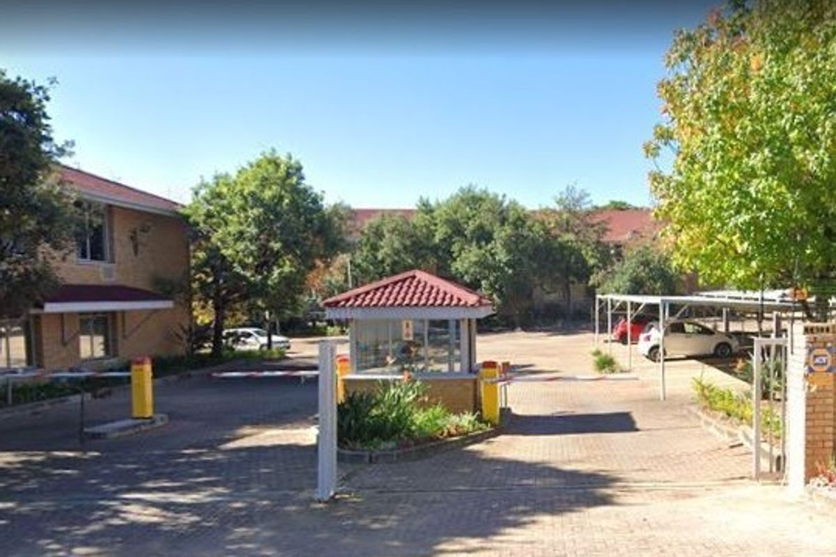 Commercial property entrance featuring a security guard booth, boom gate access control, paved driveway, and covered parking area.