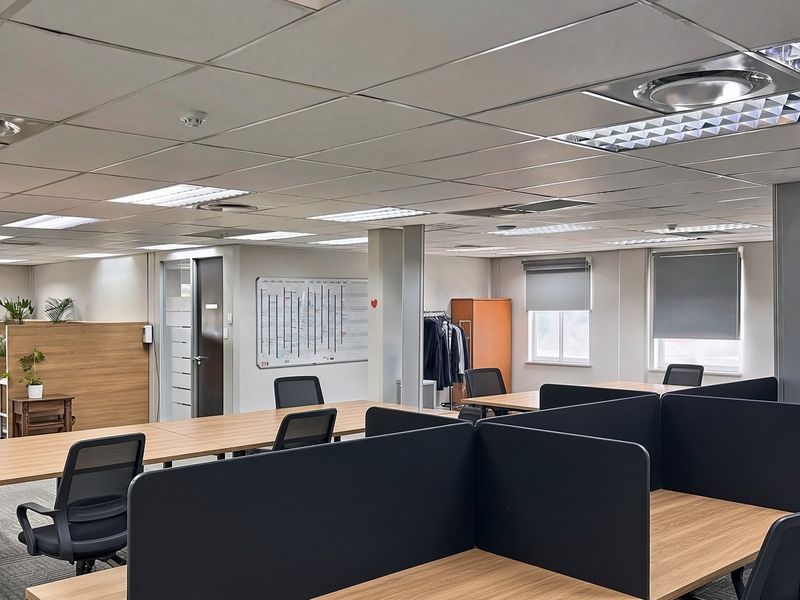 A professional open-plan office space featuring suspended ceilings, recessed lighting, carpeted flooring, and integrated partition walls for a functional workspace environment.