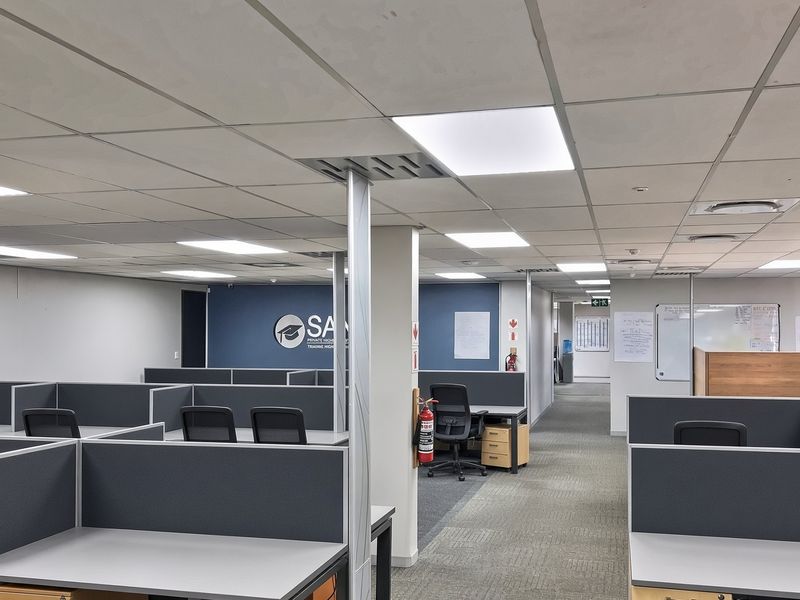 A professional open-plan office space featuring a suspended ceiling with recessed lighting, carpeted flooring, and integrated air conditioning systems.