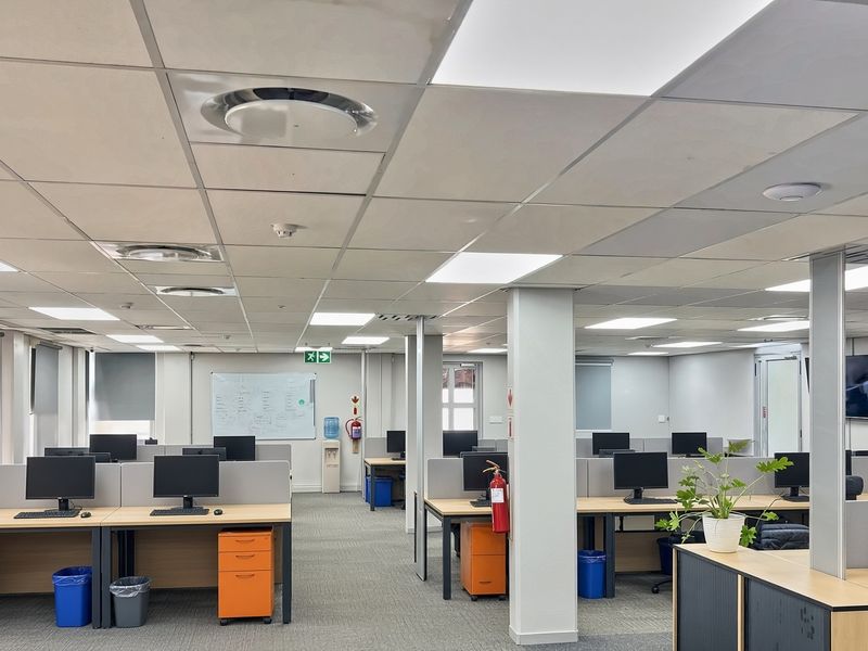 A professional open-plan office space featuring modular workstations, suspended ceilings with integrated lighting, and neutral carpeting throughout.
