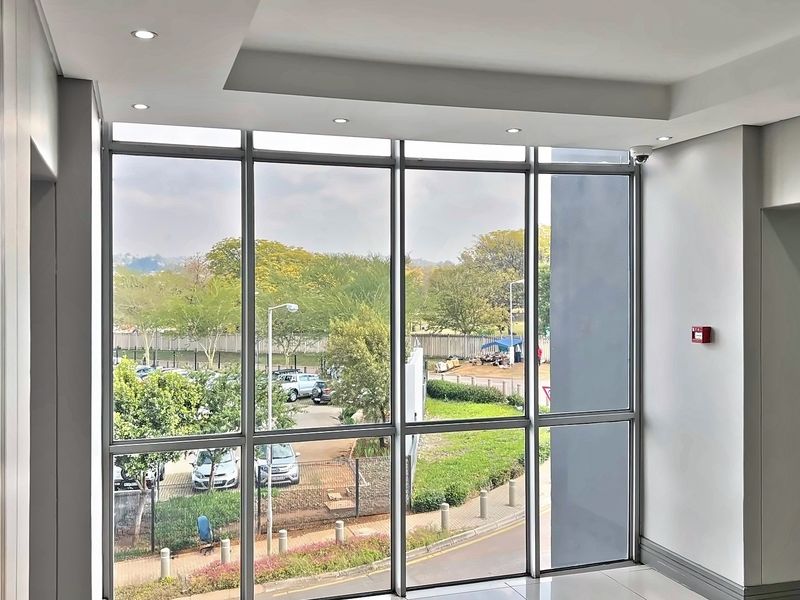 A bright, modern commercial hallway featuring expansive floor-to-ceiling windows, recessed lighting, and a clean, professional finish.
